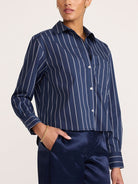 A model wearing a navy blue and white vertically striped cropped button-down shirt with dark navy pants, shown from the neck down against a plain light background.
