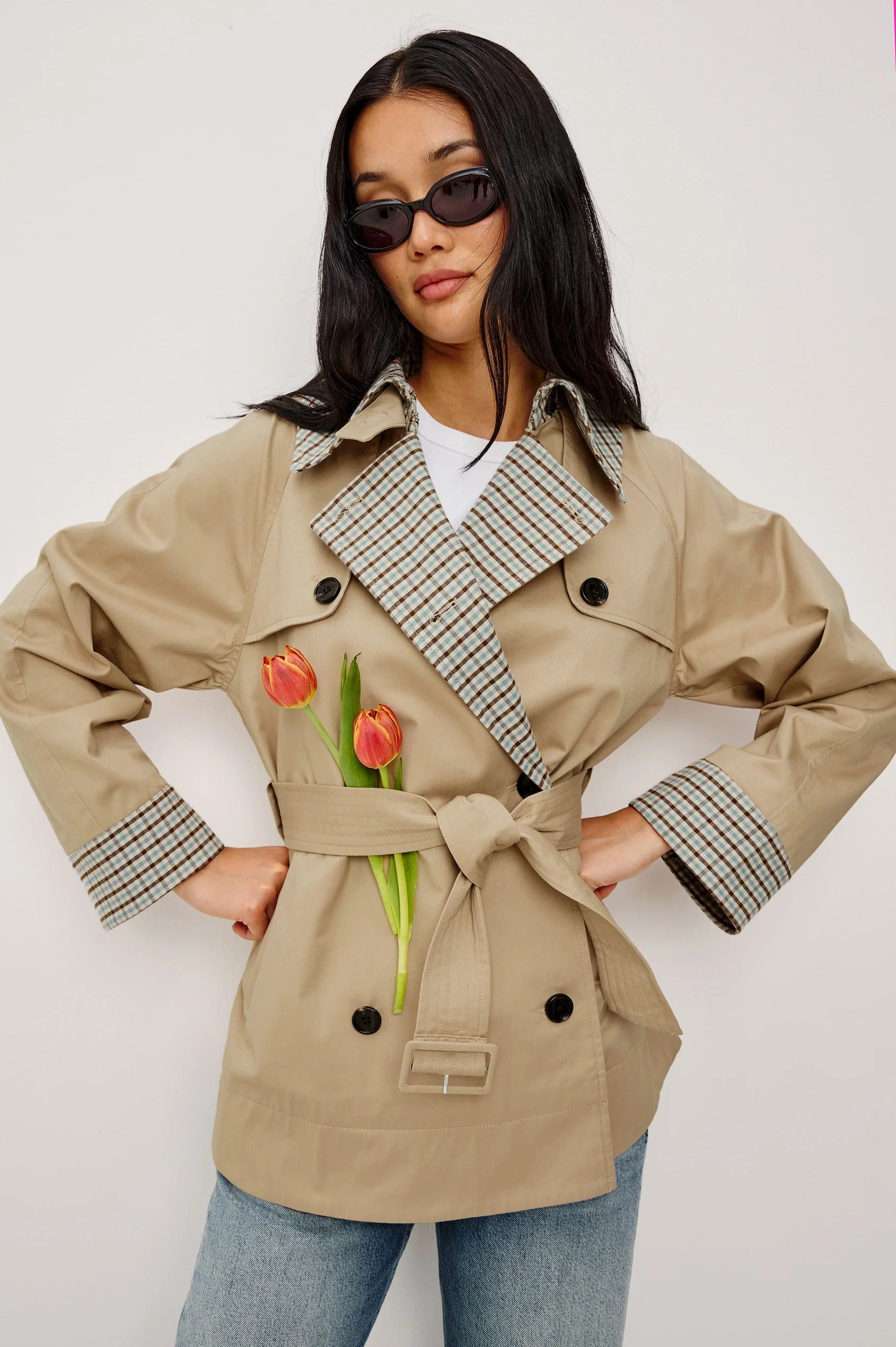 Woman wearing a beige trench coat with plaid accents on a white background
