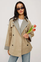Woman wearing a beige trench coat with plaid accents, holding a tulip against a white background