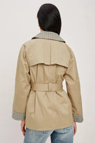 Person wearing a beige trench coat with plaid collar and cuffs on a white background