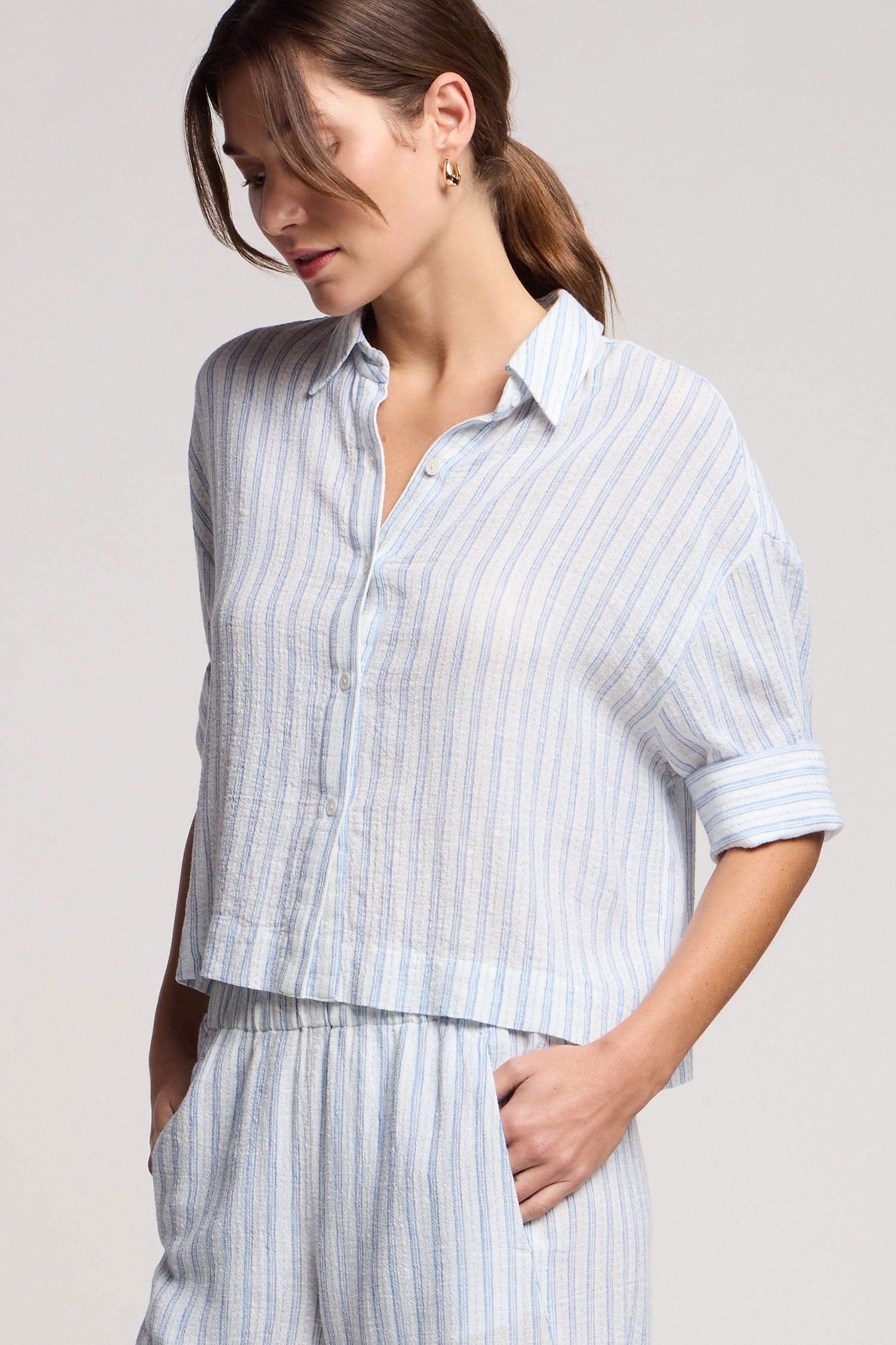 Woman wearing a light blue and white striped shirt and pants on a plain background