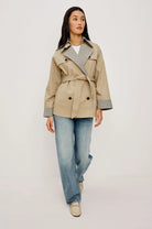 Woman wearing a beige trench coat with plaid accents on a plain background