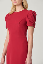 A woman wearing a red fit-and-flare dress with short puff sleeves, shown from the shoulders to the knees against a light gray studio background.