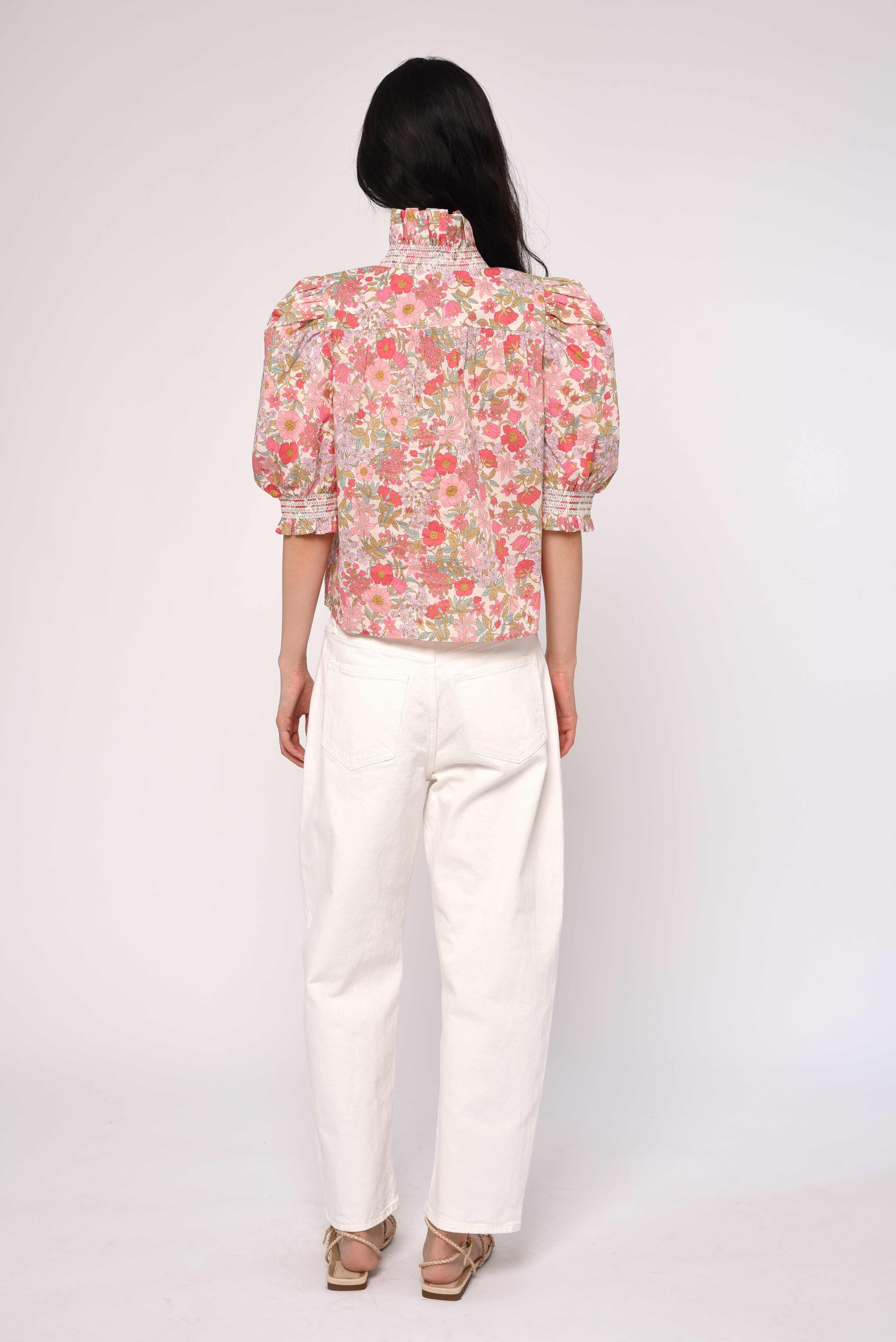 Person wearing a floral blouse and white pants on a plain background