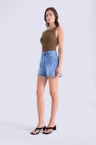 Woman wearing a brown sleeveless top and blue denim shorts on a white background