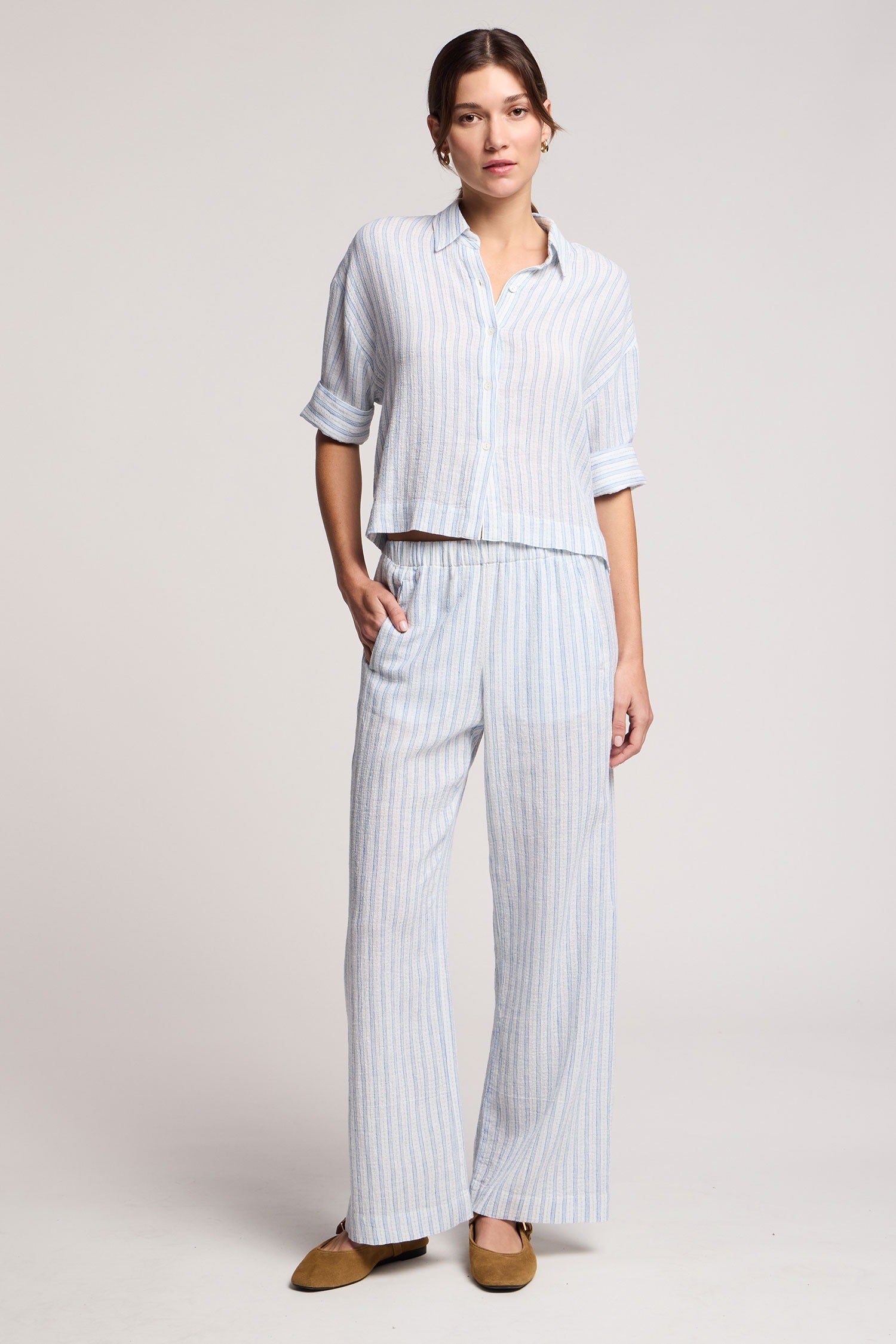 Woman wearing a light blue striped shirt and wide-leg pants on a plain background