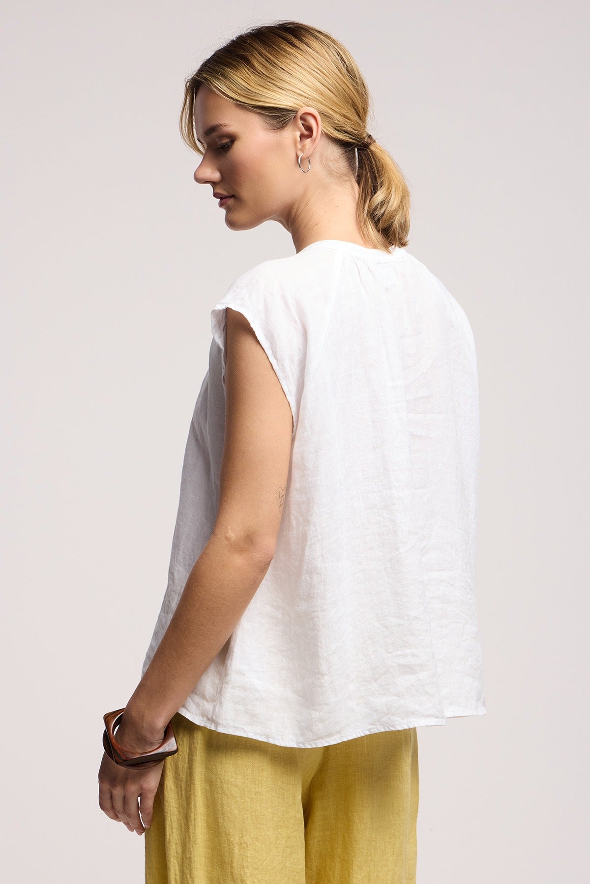 Woman wearing a white sleeveless top and yellow pants on a light gray background