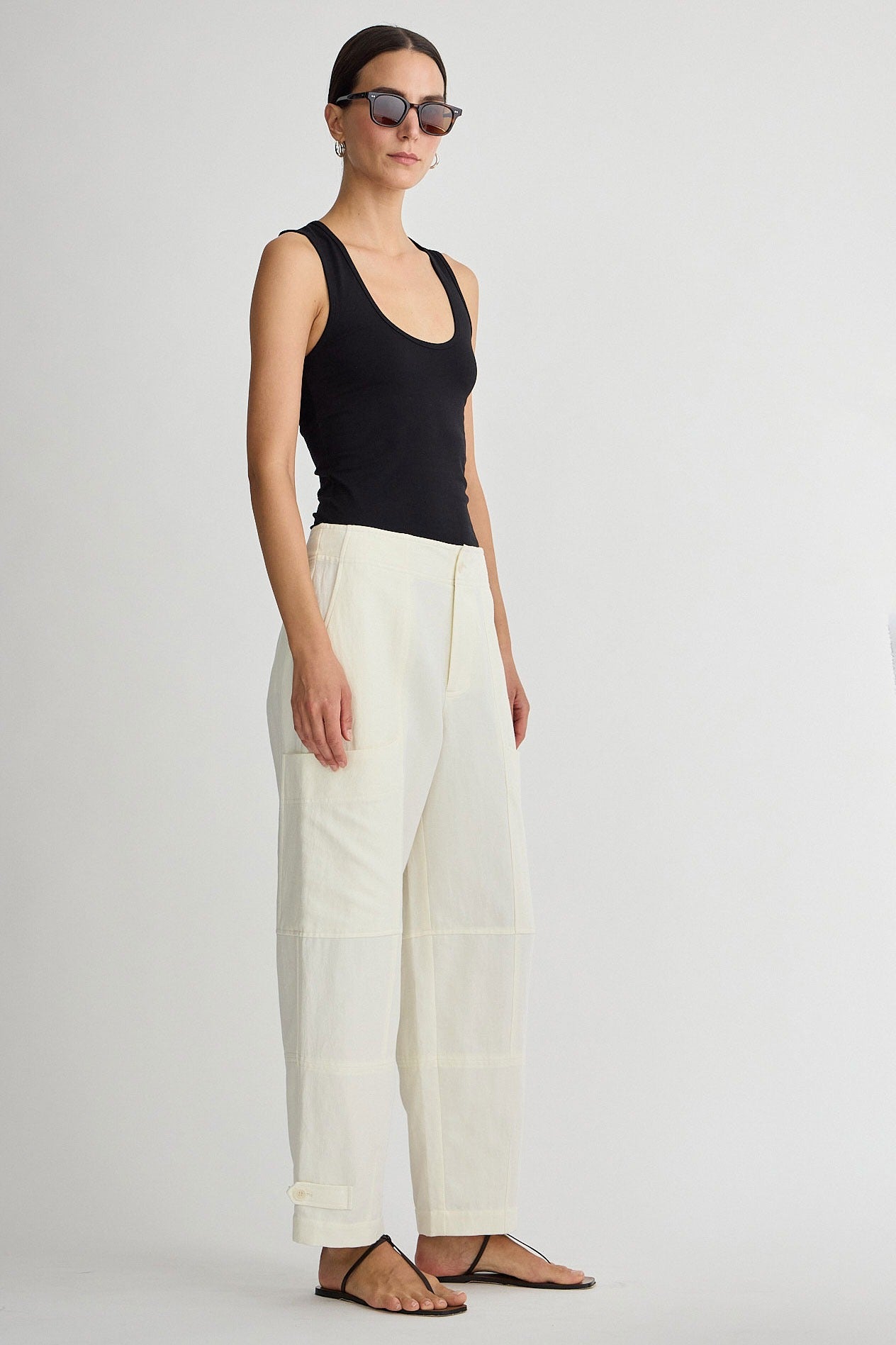 Woman wearing a black tank top and white pants on a plain background