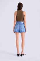Person wearing a brown sleeveless top and blue denim shorts on a white background