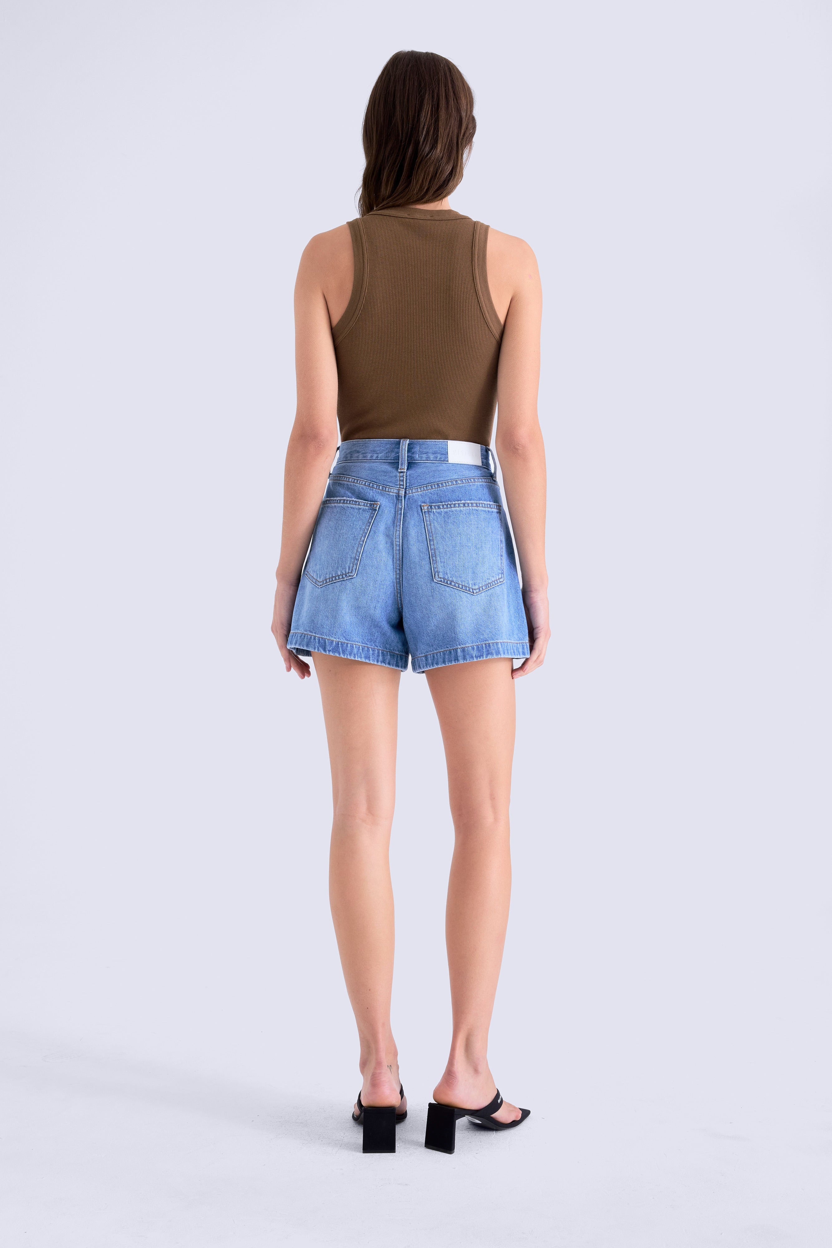 Person wearing a brown sleeveless top and blue denim shorts on a white background
