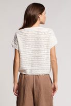 Woman wearing a white textured top and brown pants on a plain background