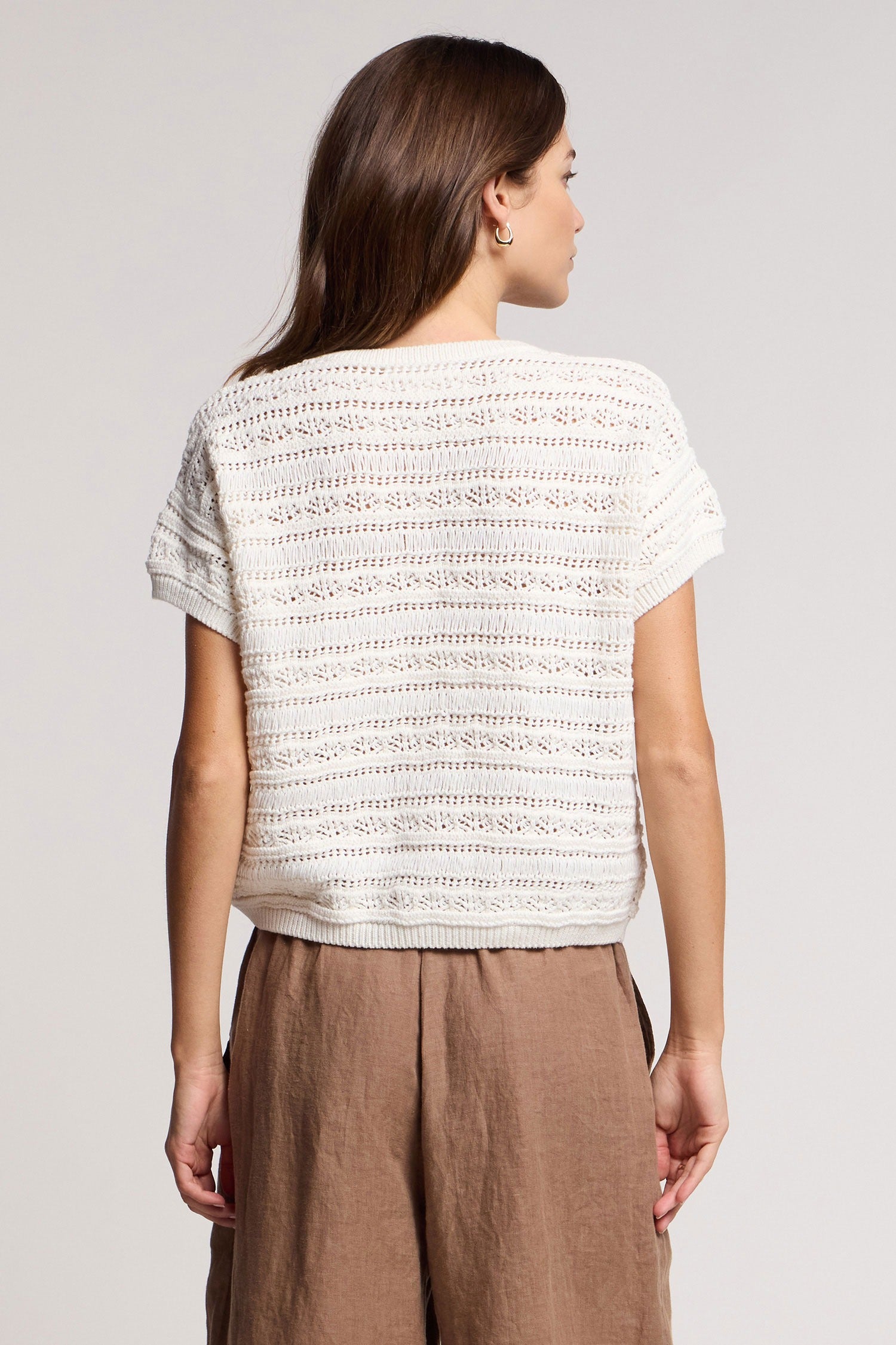 Woman wearing a white textured top and brown pants on a plain background