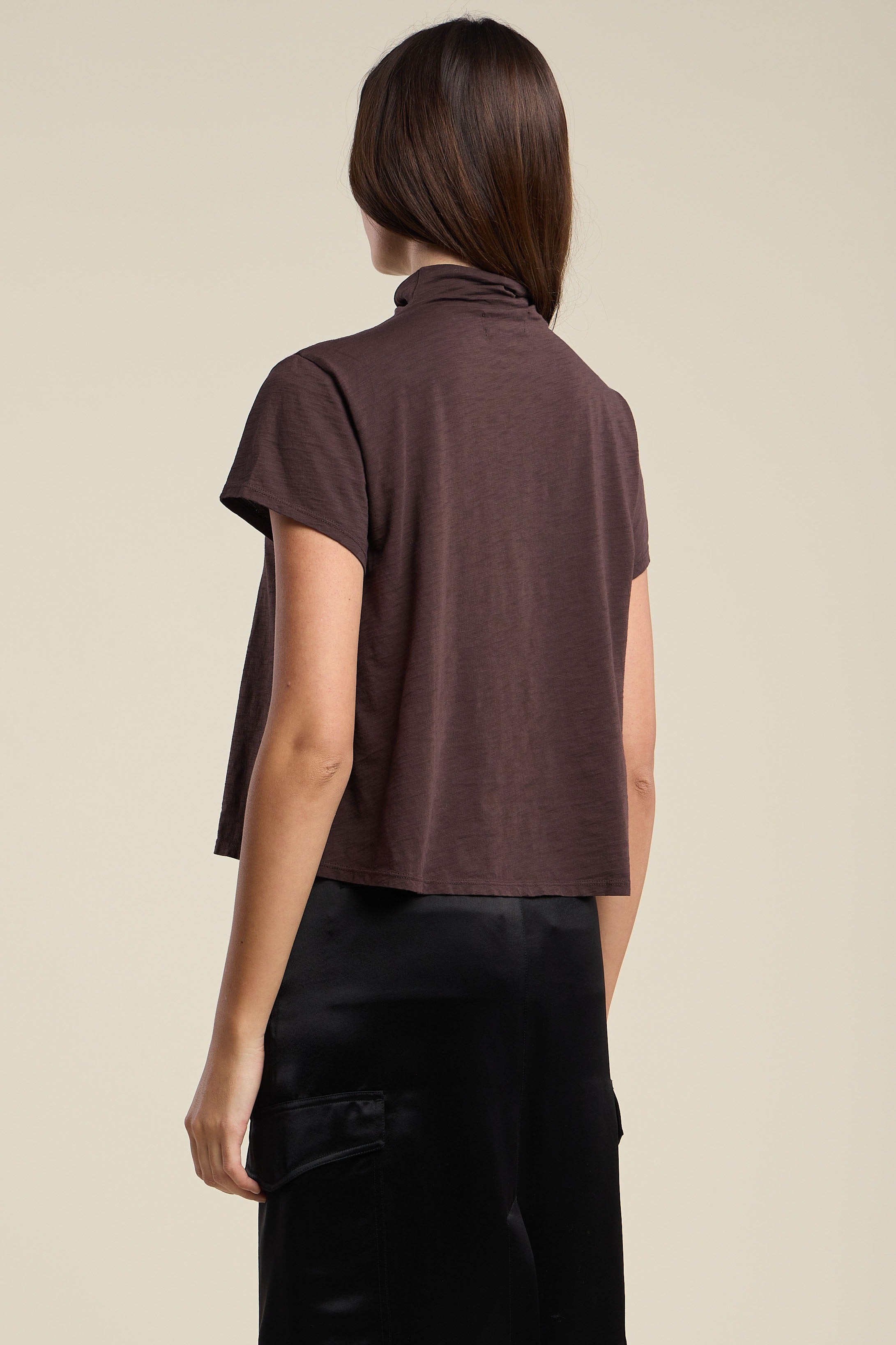 Woman wearing a brown turtleneck top and black pants on a beige background