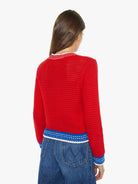 Person wearing a red crochet sweater with blue and white trim on a white background