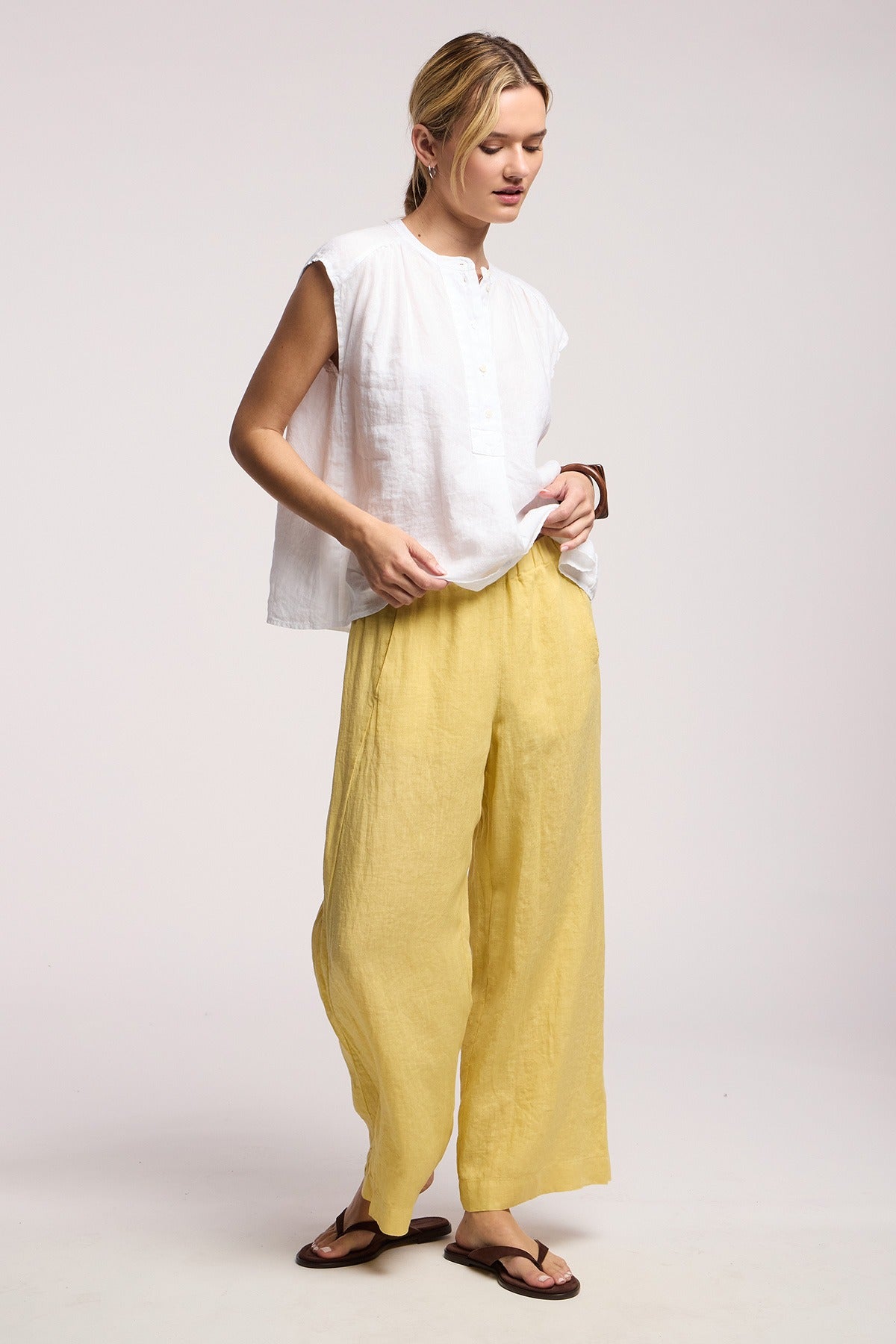 Woman wearing a white sleeveless top and yellow pants on a plain background