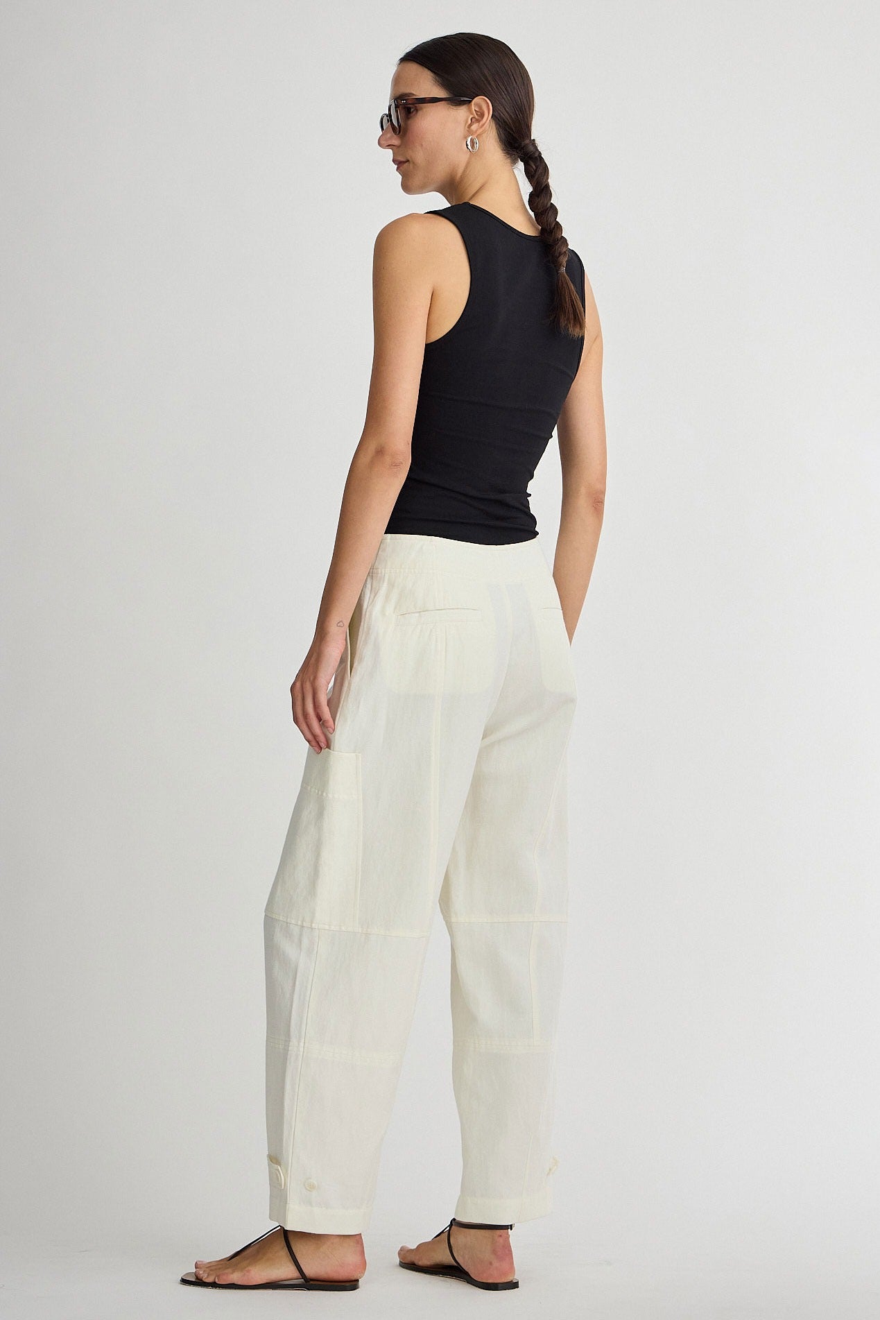 Woman wearing a black sleeveless top and white pants on a plain background