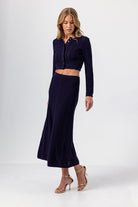 Woman wearing a navy blue outfit with a cropped top and long skirt on a white background