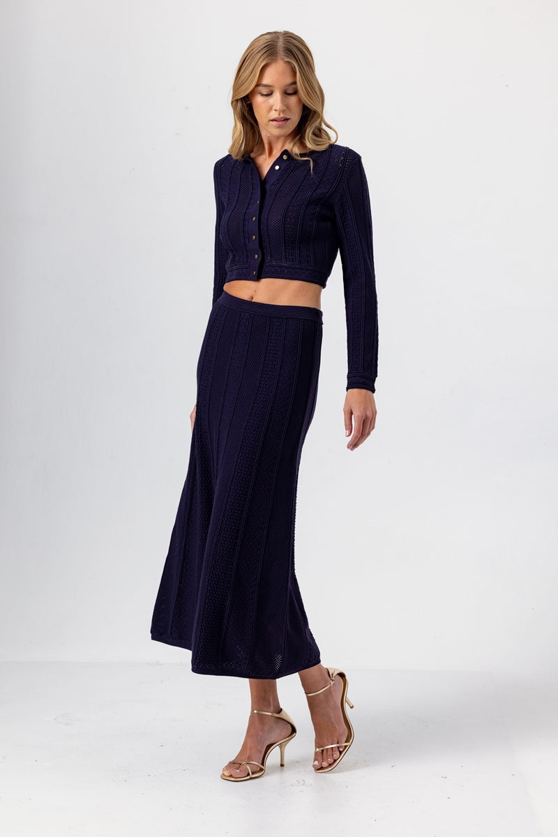 Woman wearing a navy blue outfit with a cropped top and long skirt on a white background