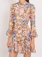 A long-sleeve mini dress with a multicolor floral and leopard print pattern, featuring a high ruffled collar, a self-tie waist belt, and flared bell sleeves, shown on a model against a plain light background.