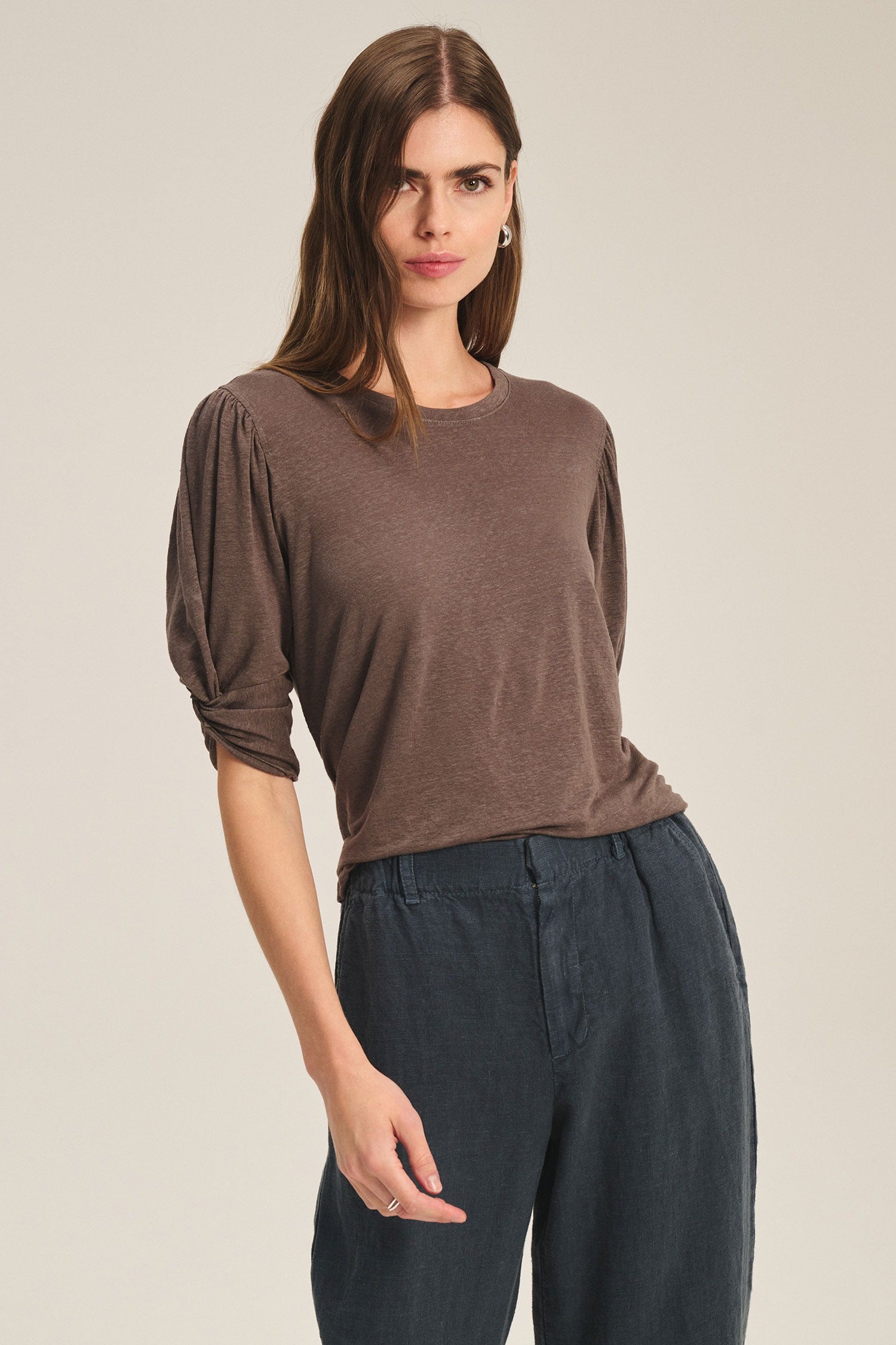 Woman wearing a brown top and dark pants against a beige background