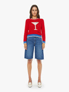 Woman wearing a red sweater with a martini glass design and blue denim shorts on a white background