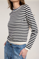 Person wearing a black and white striped sweater with blue jeans on a plain background