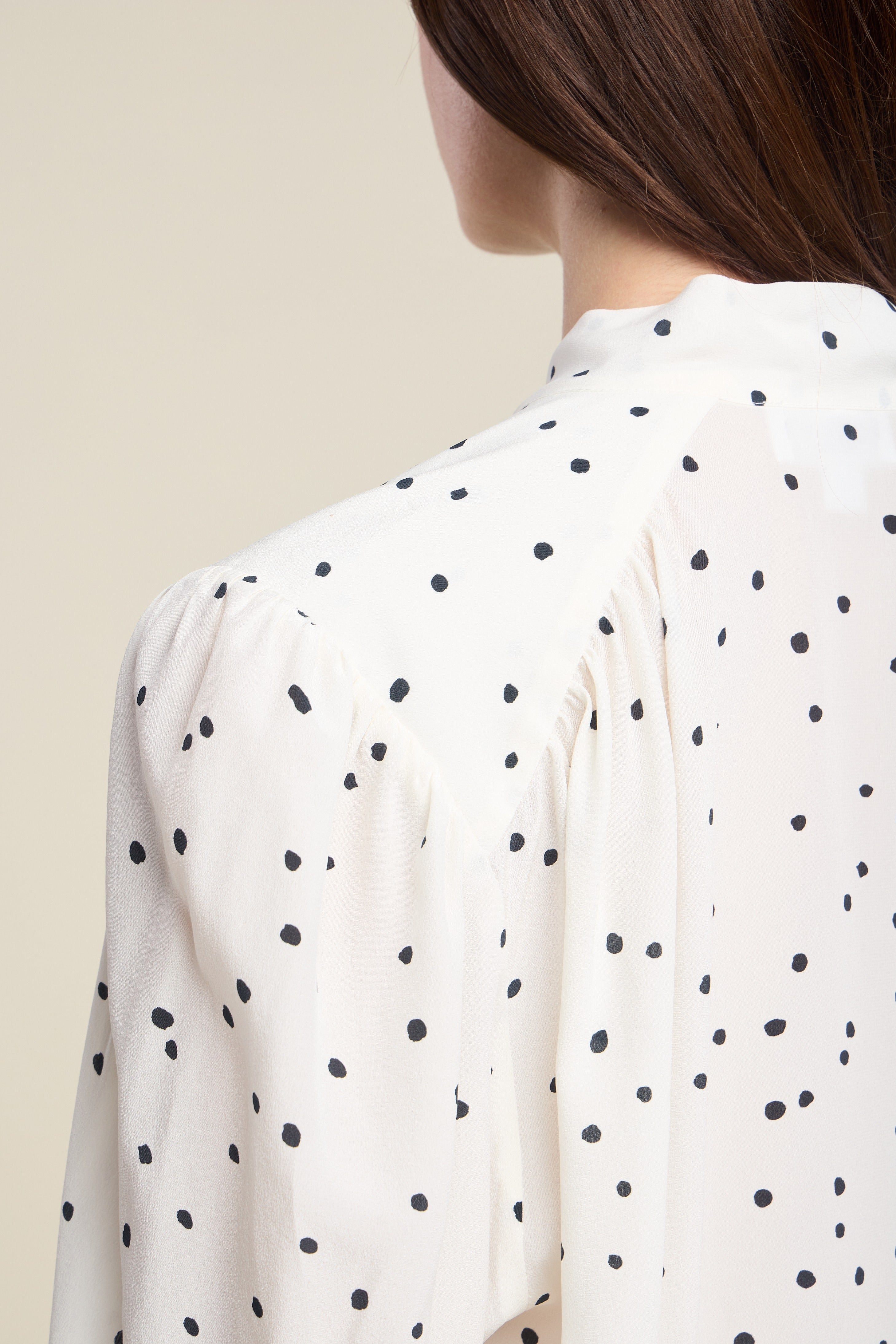 White blouse with black polka dots worn by a person against a beige background