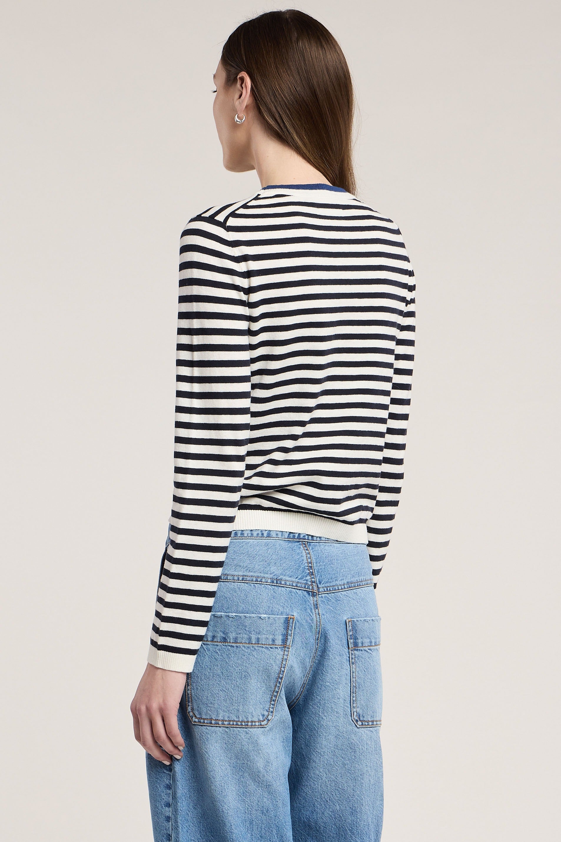 Person wearing a black and white striped long-sleeve top and blue jeans on a plain background
