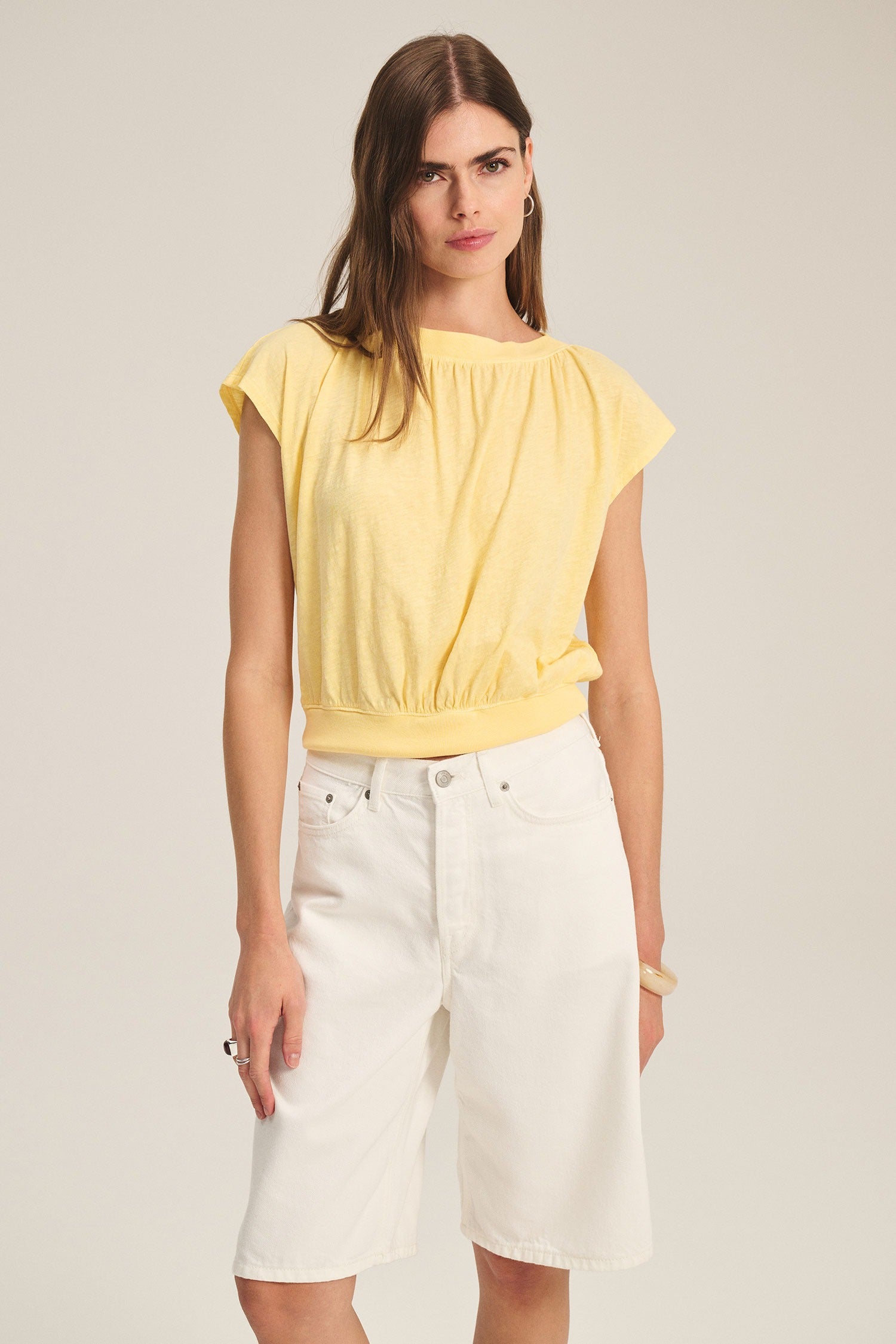 Woman wearing a yellow top and white shorts on a plain background
