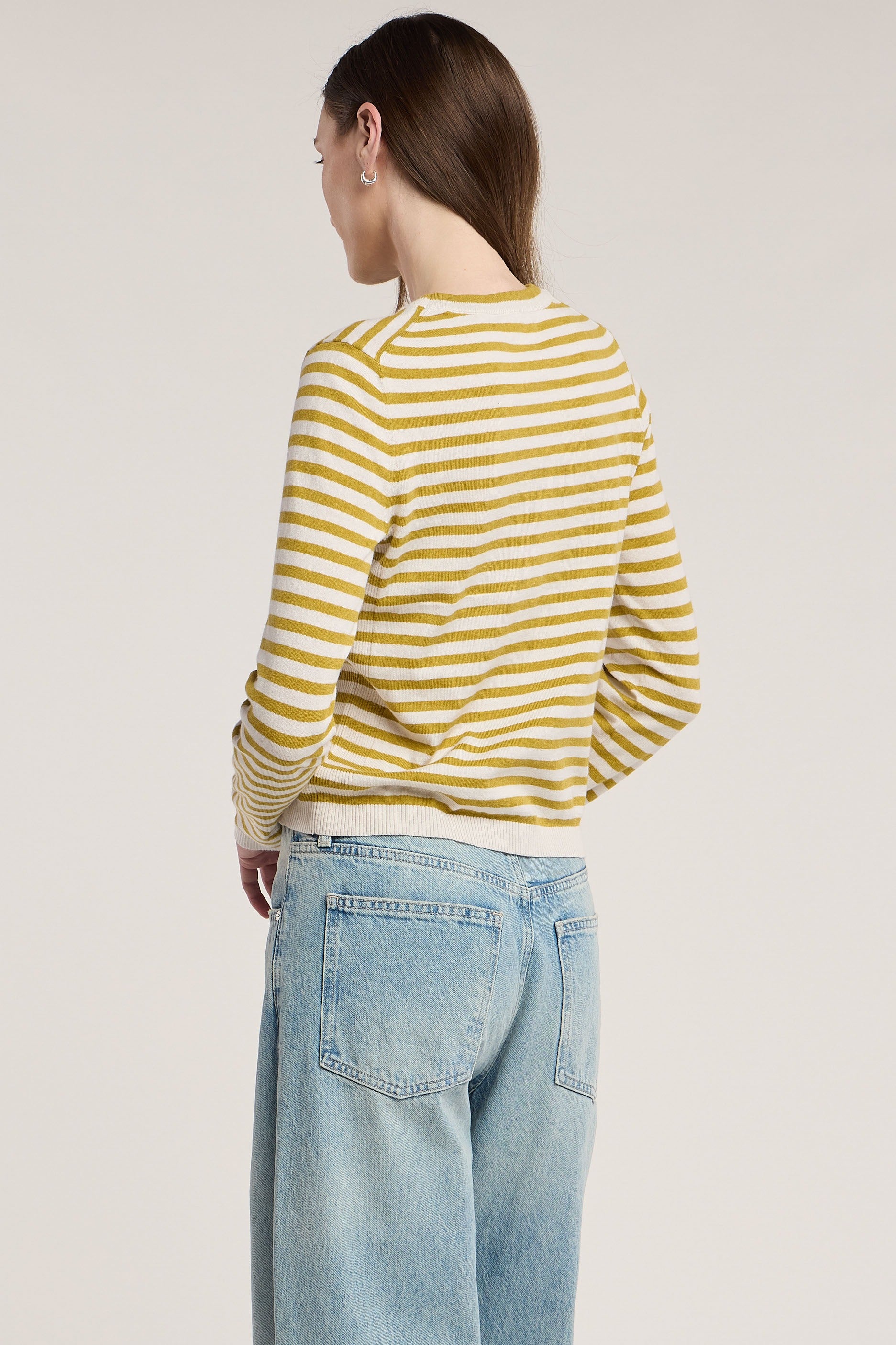 Person wearing a yellow and white striped shirt and light blue jeans on a plain background