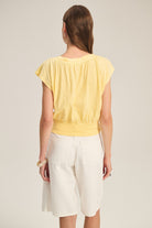 Woman wearing a yellow top and white pants on a plain background