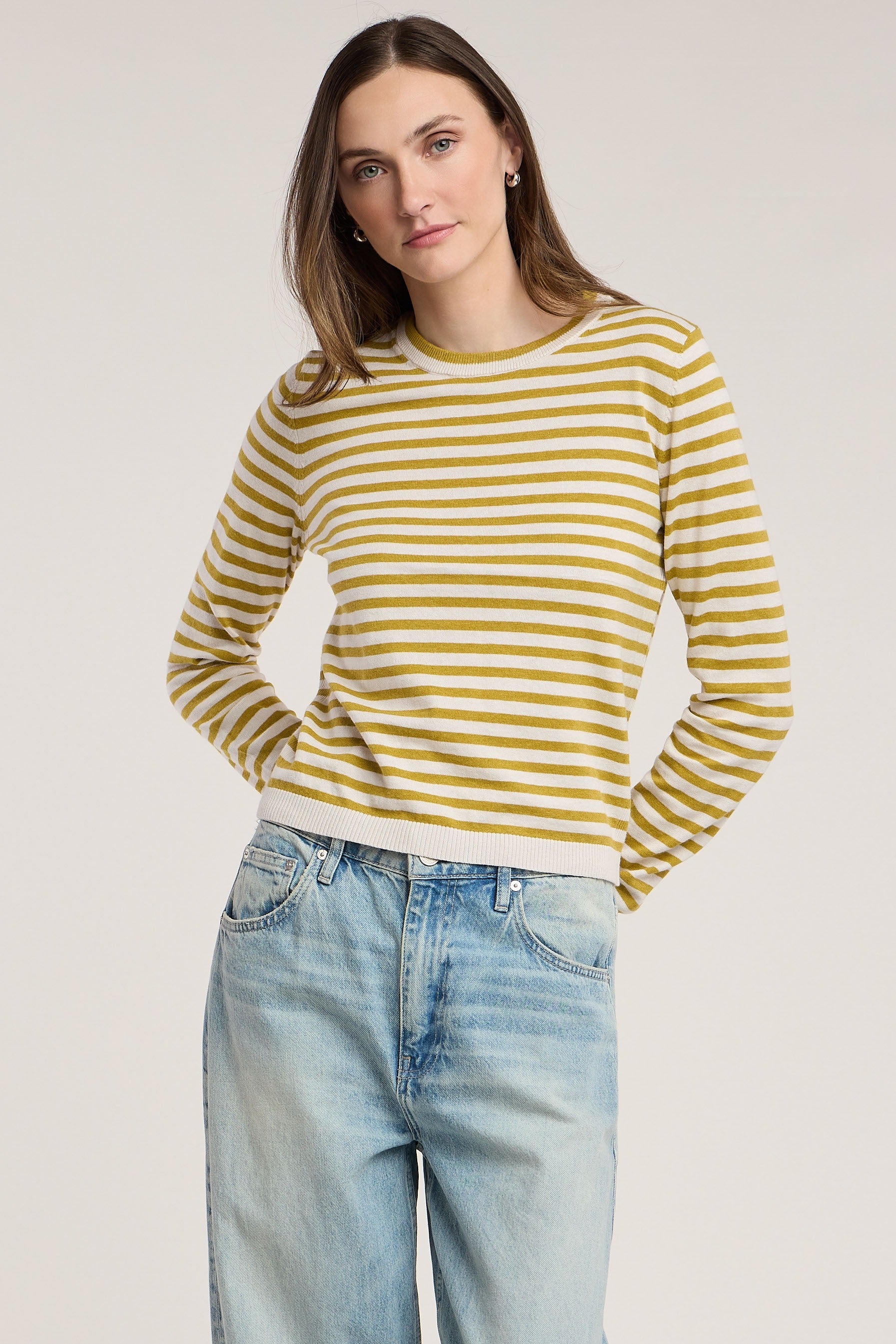 Woman wearing a yellow and white striped sweater with blue jeans on a plain background