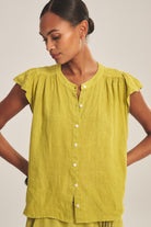 Woman wearing a green blouse with button details on a plain background