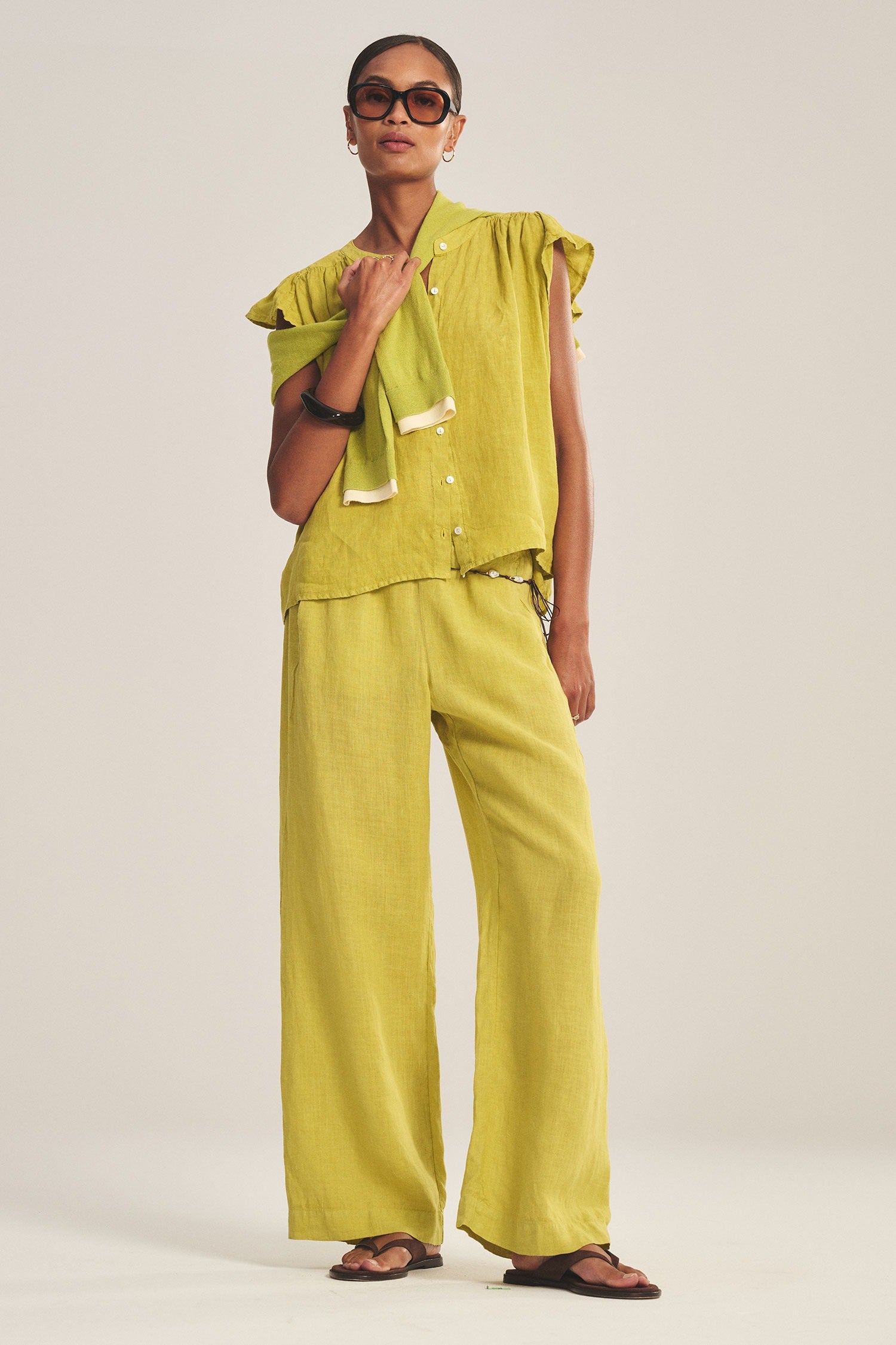 Woman wearing a green outfit with sunglasses on a plain background