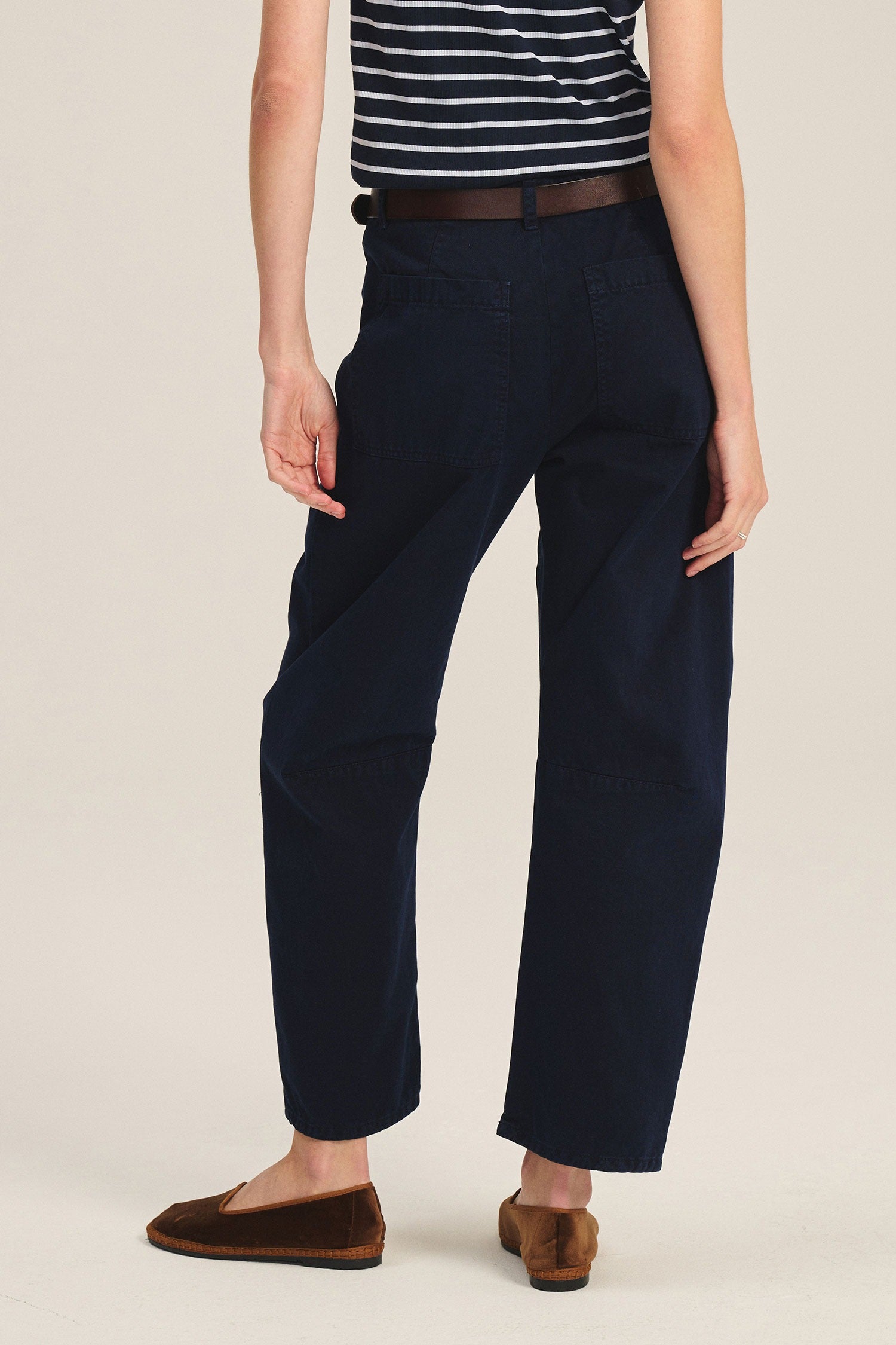 Person wearing navy pants and a striped shirt on a beige background