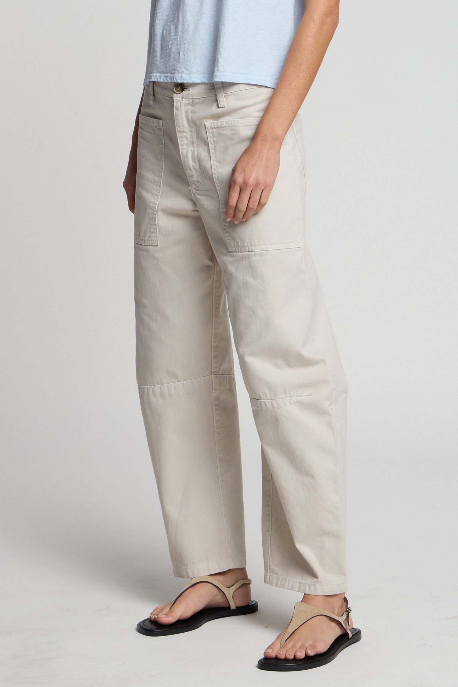 Person wearing beige pants and black sandals on a plain background