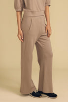 A model wearing a matching taupe beige two-piece set consisting of a short-sleeve cropped top and high-waisted wide-leg pants, paired with navy blue slip-on shoes, against a solid beige background.