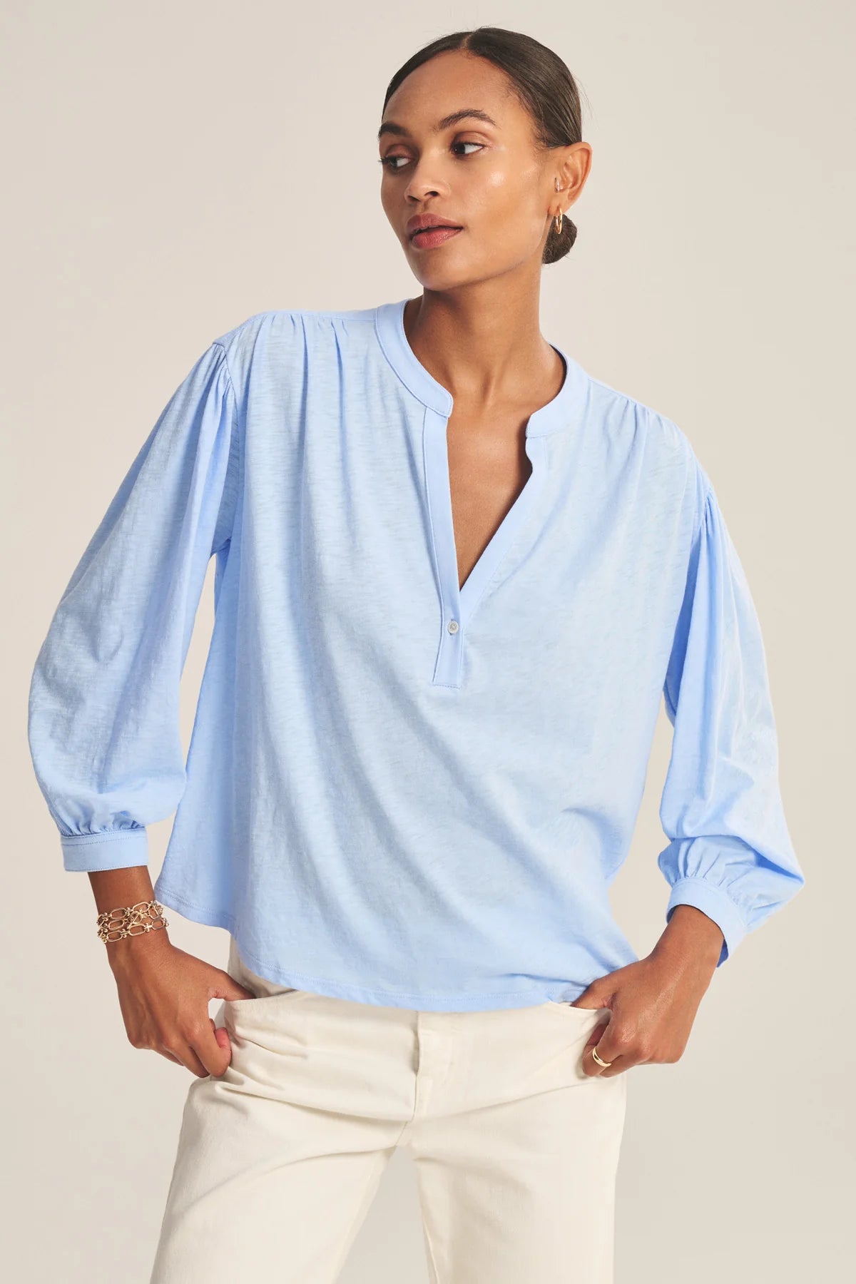 Woman wearing a light blue blouse with long sleeves against a neutral background