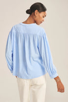 Woman wearing a light blue blouse with long sleeves on a beige background