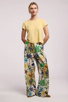 Woman wearing a yellow top and colorful patterned pants on a light background