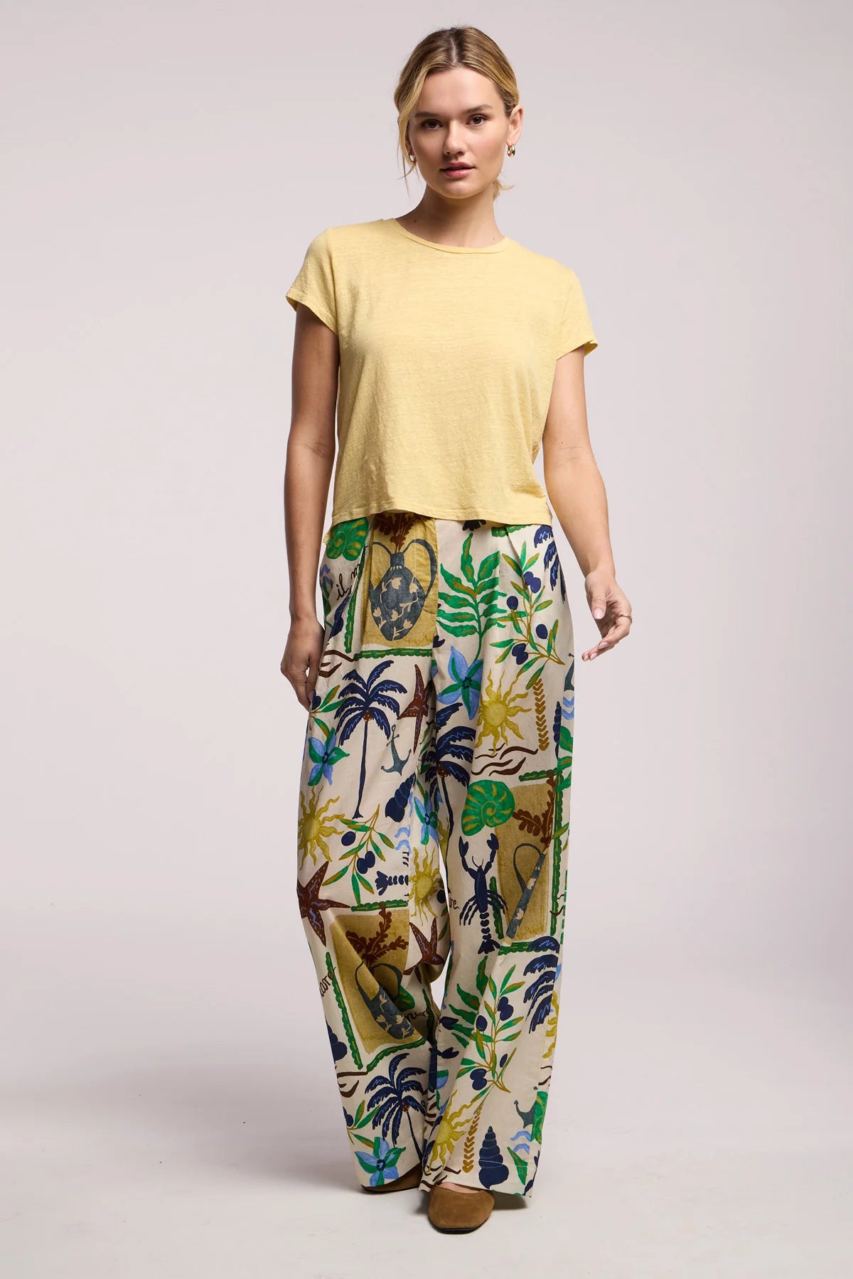 Woman wearing a yellow top and colorful patterned pants on a light gray background