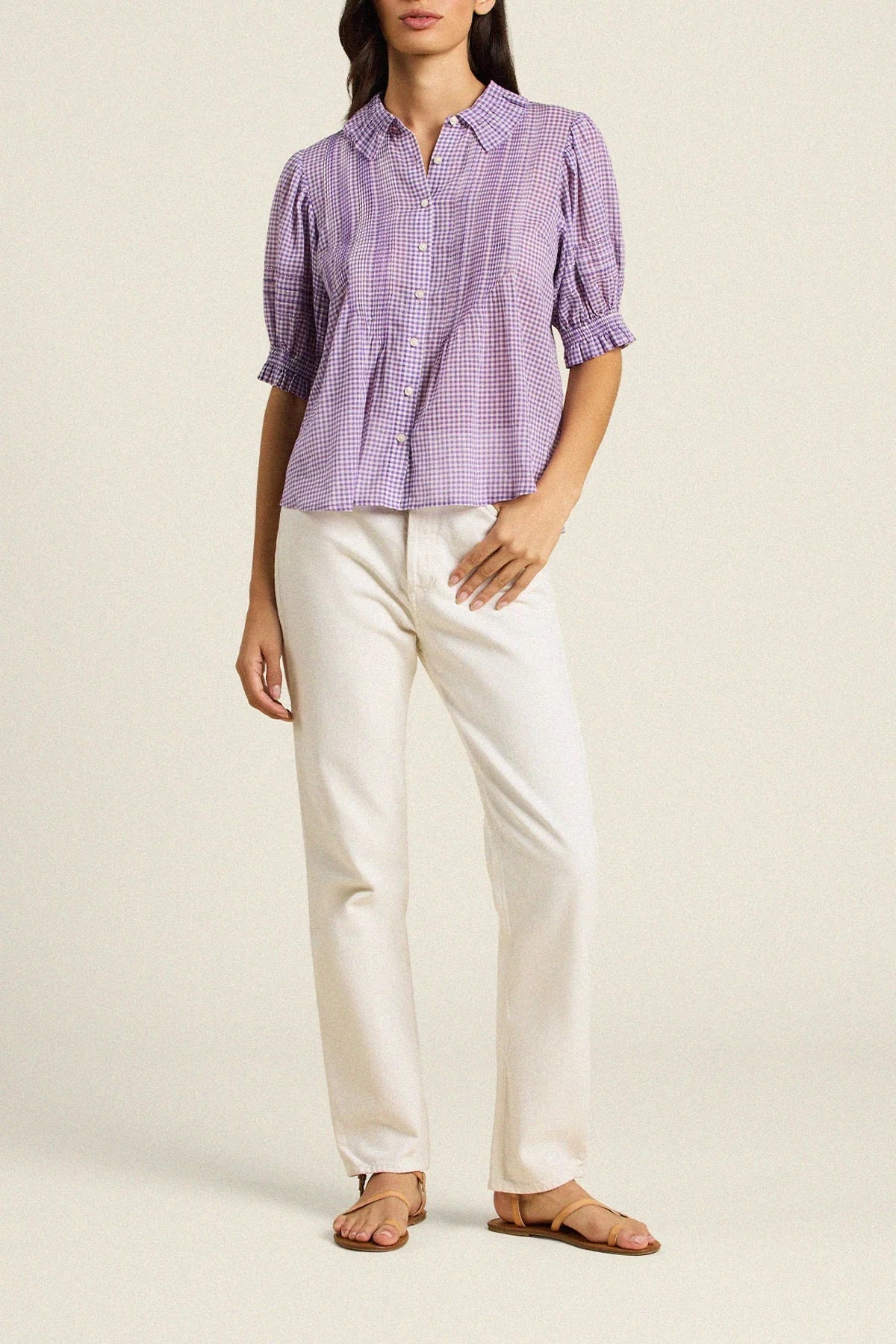 Woman wearing a purple checkered shirt and white pants on a beige background