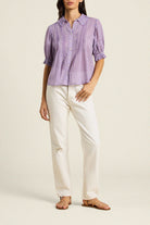 Woman wearing a purple checkered shirt and white pants on a beige background