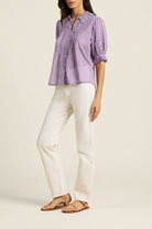 Woman wearing a purple checkered shirt and white pants on a beige background