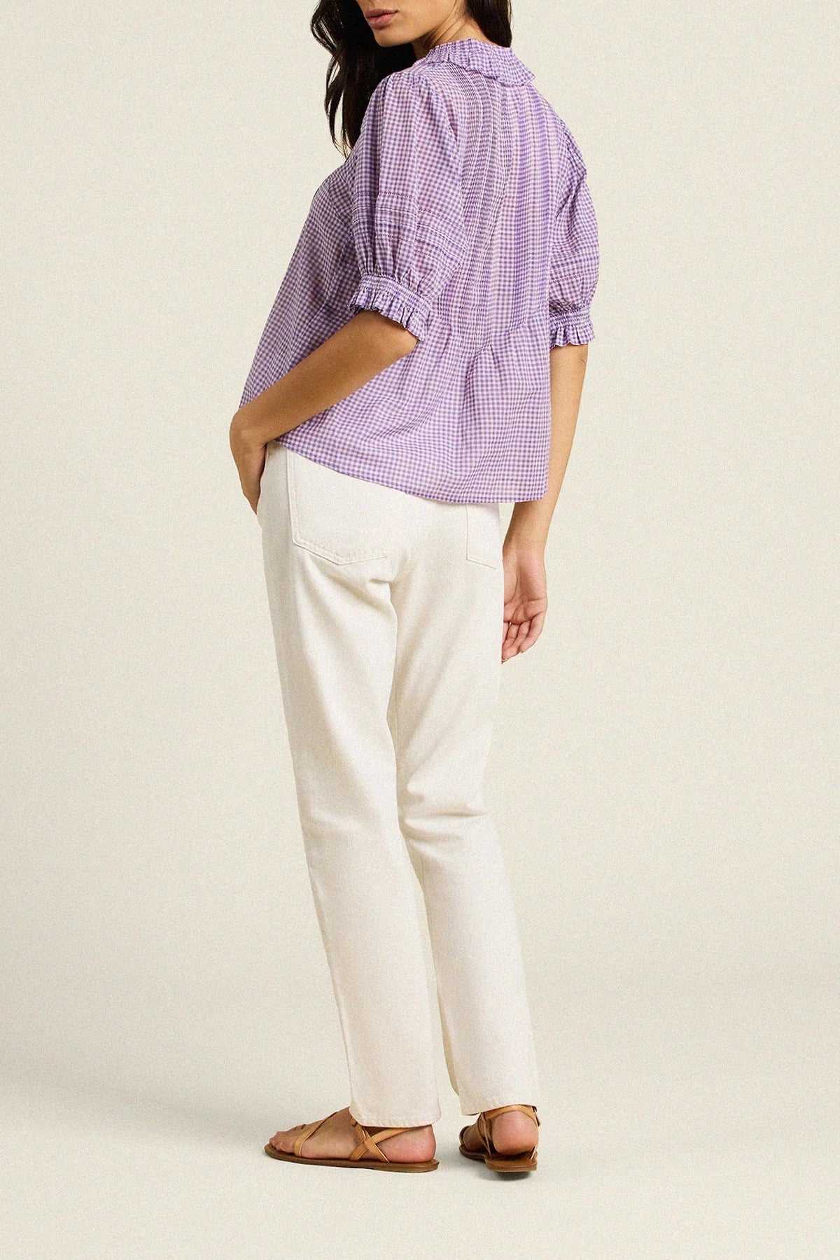 Woman wearing a purple checkered shirt and white pants on a beige background