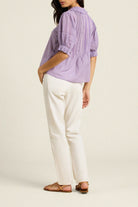 Woman wearing a purple checkered shirt and white pants on a beige background