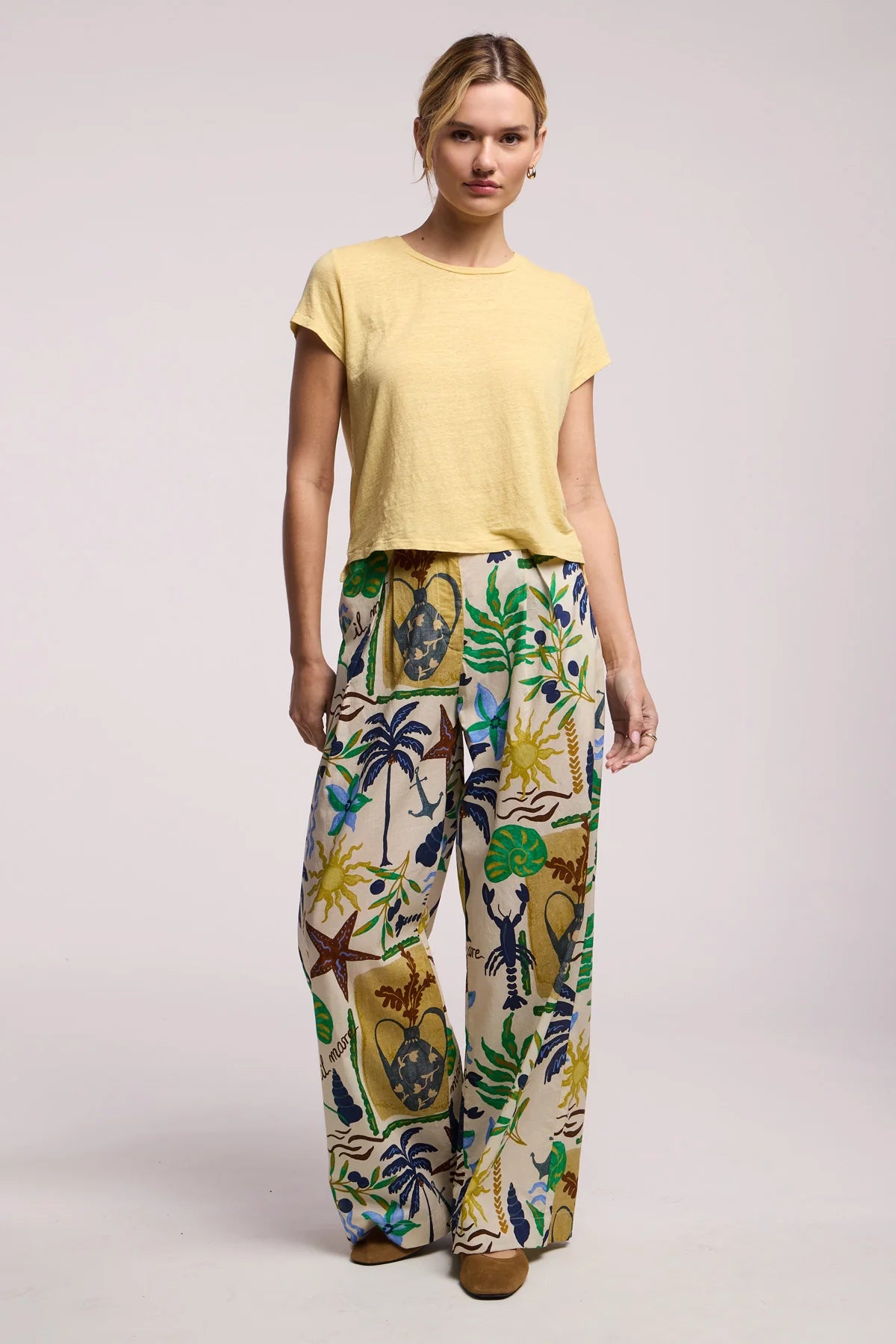 Woman wearing a yellow top and colorful patterned pants on a light gray background