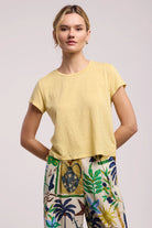Woman wearing a yellow top and colorful pants on a plain background