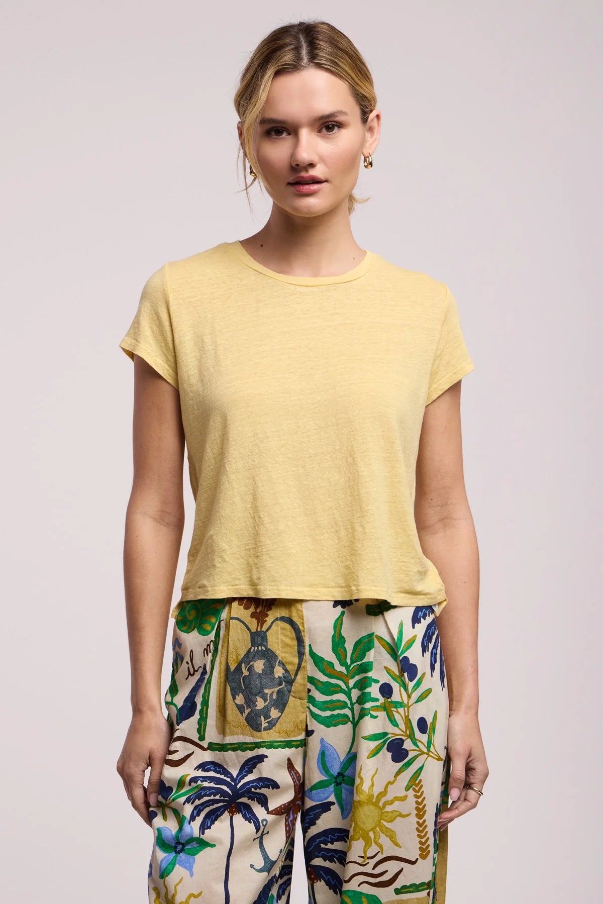 Woman wearing a yellow top and colorful pants on a light background