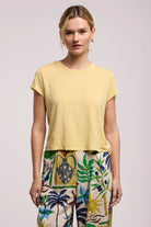 Woman wearing a yellow top and colorful pants on a light background